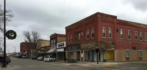 A quiet street scene featuring brick buildings, a wreath on a lamp post, and overcast skies.