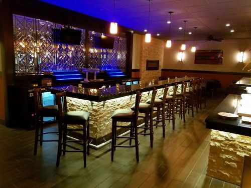 A modern bar with stone accents, high stools, and blue lighting, featuring a sleek countertop and wall decor.