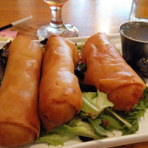 Three crispy spring rolls on a bed of lettuce, served with a small container of dipping sauce.