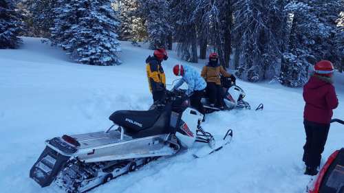 Two snowmobiles in a snowy landscape with people preparing for a ride in a winter setting.