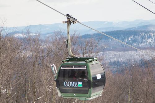 A green gondola labeled "GORE" suspended over a snowy landscape with mountains in the background.