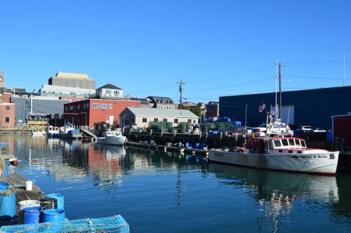 A calm harbor scene with boats docked, colorful buildings, and clear blue skies reflecting on the water.