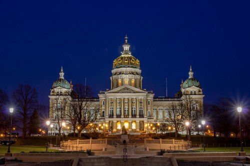 Iowa State Capitol building illuminated at night, showcasing its golden dome and ornate architecture against a dark sky.
