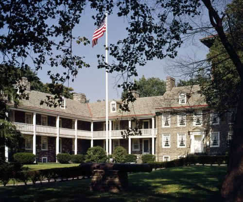 Historic building with a flagpole, surrounded by trees and a cannon in the foreground, showcasing classic architecture.