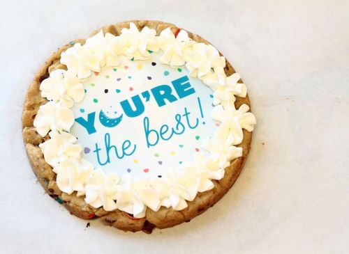 A large cookie decorated with white frosting and a message that says "YOU'RE the best!" surrounded by colorful sprinkles.