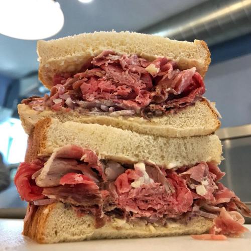 A towering sandwich filled with layers of pink deli meat between slices of soft white bread.
