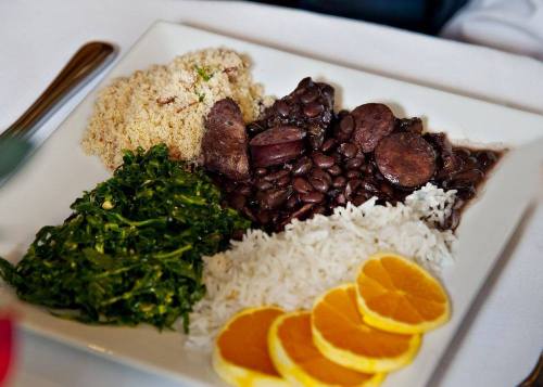 A plate of rice, black beans, greens, couscous, and orange slices, arranged neatly on a white dish.