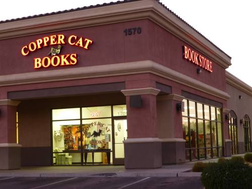 Exterior of Copper Cat Books bookstore, featuring bright signage and large windows, during twilight.