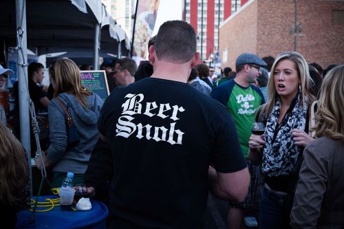 A crowd at an outdoor event, with a man wearing a "Beer Snob" shirt and a woman talking nearby.