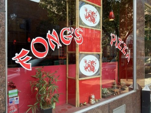 Window display of Fong's Pizza featuring red and white signage with decorative plants and bamboo accents.