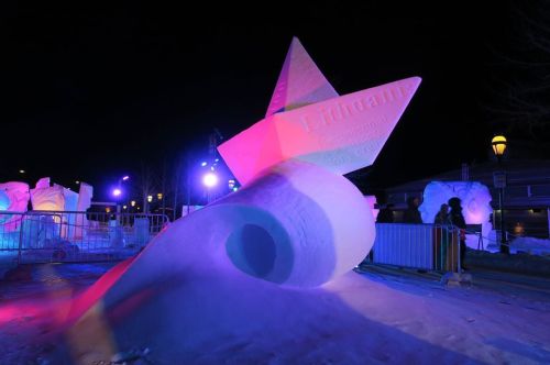 A large, illuminated snow sculpture of a boat, surrounded by snow and colorful lights at night.