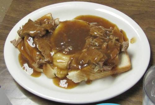 A plate of bread topped with shredded meat and brown gravy, served on a wooden table.