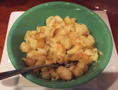 A green bowl filled with creamy macaroni and cheese, with a fork resting inside.