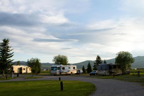 A scenic view of RVs parked in a grassy area with trees and mountains in the background under a cloudy sky.