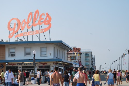 Crowd walking along a boardwalk with a large sign for "Dolle's Salt Water Taffy" in the background.
