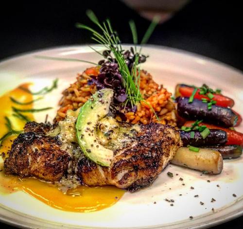 A beautifully plated dish featuring seasoned fish, vibrant rice, and colorful roasted vegetables, garnished with herbs.