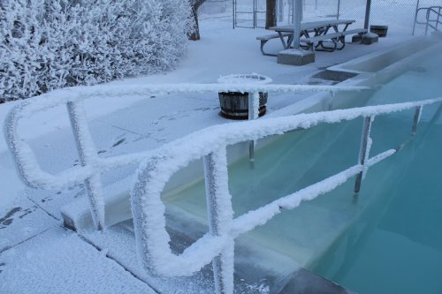 Frost-covered pool railing beside a frozen, snow-covered area with a picnic table in the background.