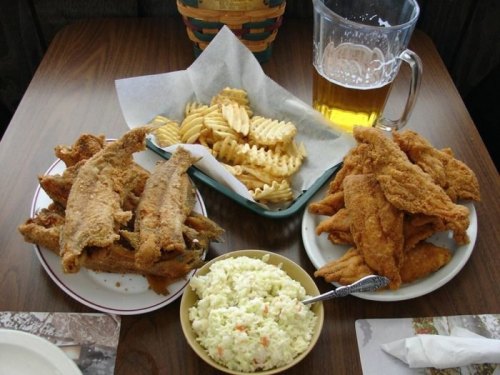 A table with fried fish, waffle fries, coleslaw, and a pitcher of beer.