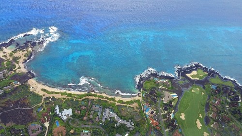 Aerial view of a coastal landscape featuring sandy beaches, turquoise waters, and a golf course along the shoreline.