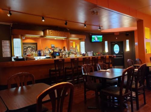 Interior of a bar with wooden tables, a well-stocked bar counter, and a TV on the wall. Warm, inviting atmosphere.