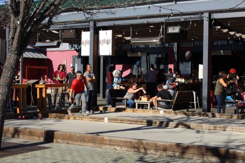 A lively outdoor dining area with people eating, socializing, and enjoying the sun at a restaurant.