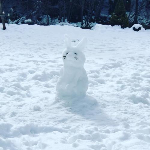 A snow sculpture of a rabbit sitting in a snowy landscape, surrounded by a blanket of white snow.