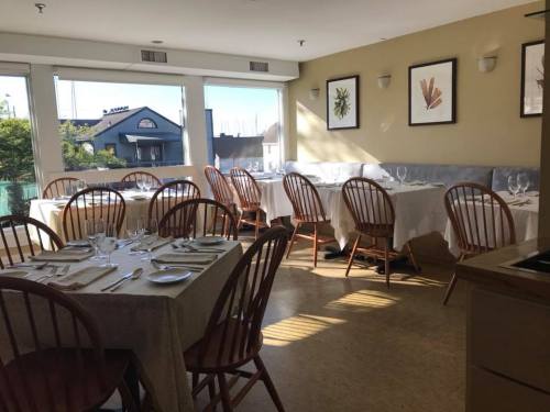 Bright restaurant interior with wooden chairs, tables set for dining, and large windows letting in natural light.