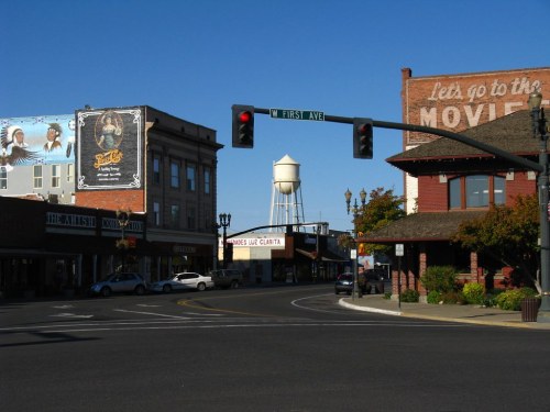 A street view featuring vintage buildings, a water tower, and a traffic light at the intersection of W First Ave.