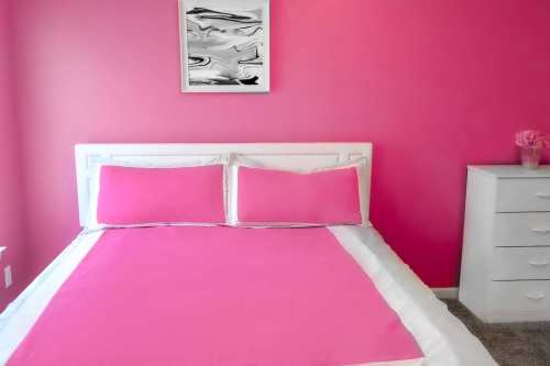 A bright pink bedroom featuring a white bed with pink pillows and a matching bedspread, alongside a white dresser.