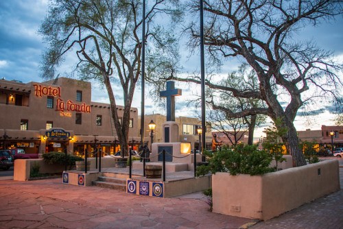 A scenic view of Hotel La Fonda at dusk, featuring a cross monument and surrounding trees.