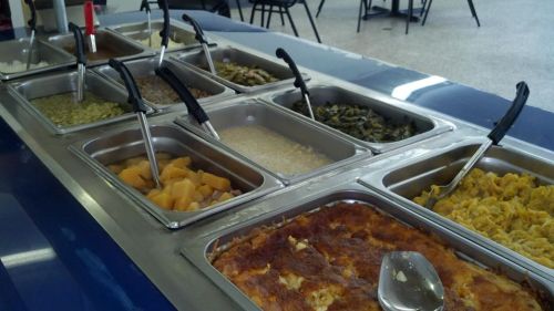 A buffet with various dishes in metal trays, including vegetables, casseroles, and sides, with serving utensils.