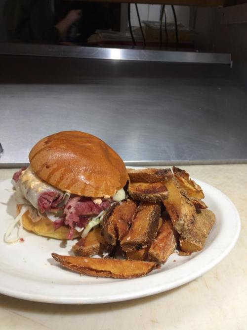 A plate with a sandwich filled with meat and toppings, accompanied by crispy potato wedges.