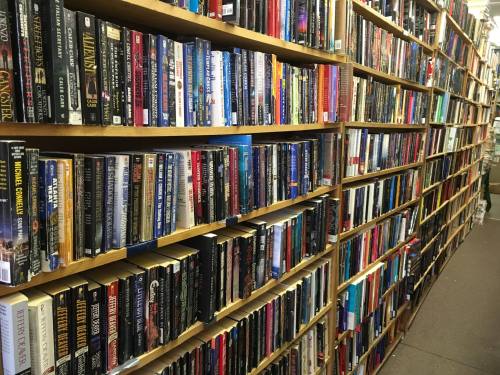 A narrow aisle between tall bookshelves filled with a variety of books in a cozy bookstore.