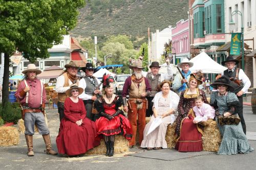 A group of people in Western-themed costumes poses on hay bales in a festive outdoor setting.