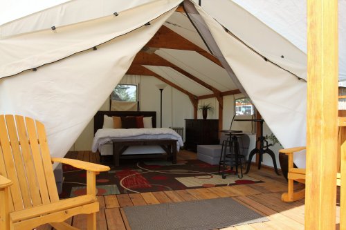Cozy glamping tent interior with a bed, seating area, and wooden deck, surrounded by natural light.