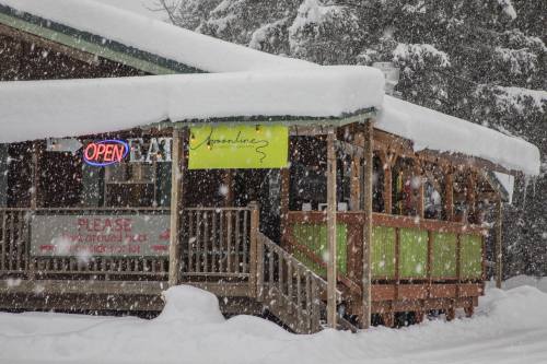 A cozy restaurant with an "Open" sign, surrounded by heavy snow and a snowy roof, inviting customers inside.