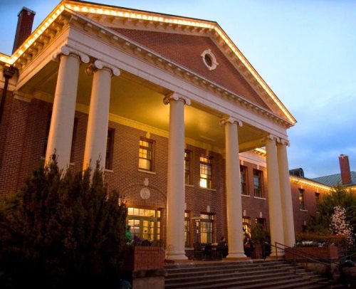 Historic building with large columns, warm lighting, and steps leading to the entrance, set against a twilight sky.