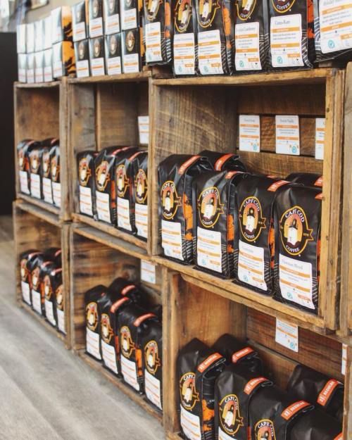 Shelves filled with bags of coffee, each labeled with different flavors and branding, in a rustic wooden display.