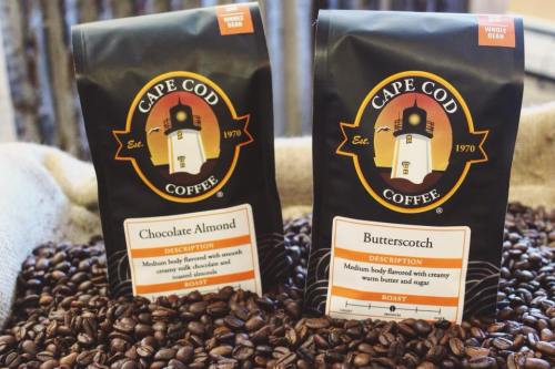 Two bags of Cape Cod Coffee, labeled Chocolate Almond and Butterscotch, surrounded by coffee beans.
