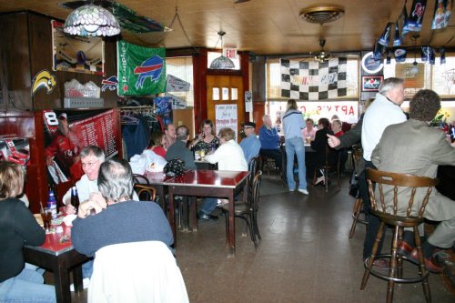 A lively bar scene with patrons socializing at tables, sports memorabilia on the walls, and a bartender serving drinks.