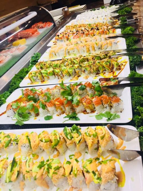 A colorful display of various sushi rolls arranged on white plates, garnished with herbs and sauces.