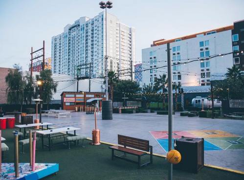 Urban outdoor space with colorful seating, string lights, and a backdrop of buildings and a train.