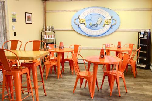 Brightly colored café interior with orange tables and chairs, featuring a Cape Cod Coffee sign on the wall.