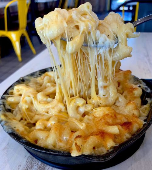 A cheesy, baked macaroni and cheese dish with gooey cheese stretching from a spoon.