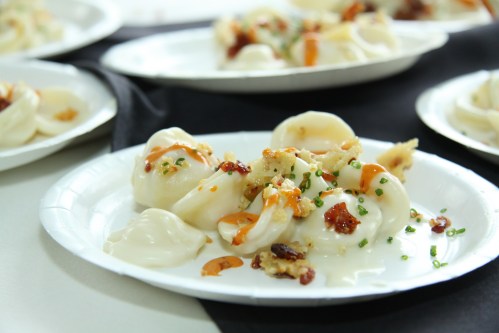 Plates of dumplings topped with crispy bits and drizzled sauce, garnished with chives on a black tablecloth.