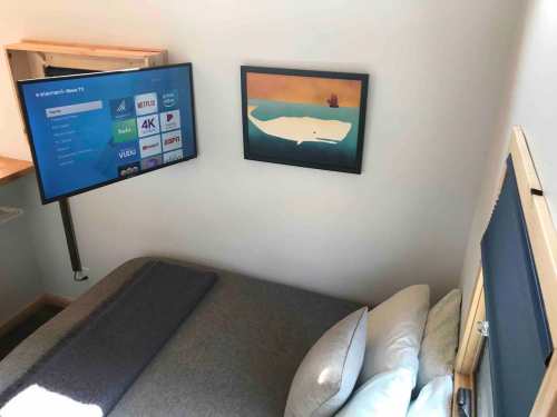Cozy room with a bed, a mounted TV displaying streaming options, and a framed painting on the wall.