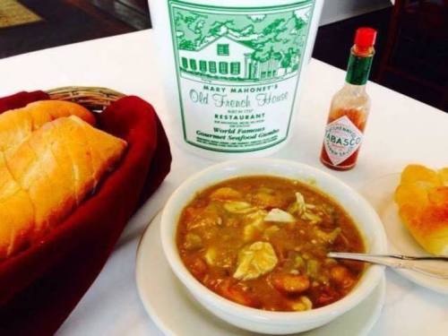 A bowl of gumbo with chicken, served with bread and a bottle of Tabasco sauce on a table.