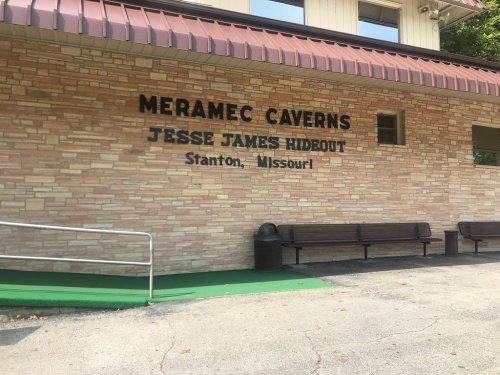 Sign on a stone wall reading "Meramec Caverns, Jesse James Hideout, Stanton, Missouri," with benches in front.