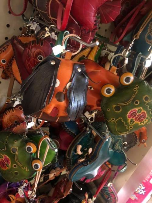 Colorful leather keychains shaped like animals, including a frog and a whimsical face, hanging on a display.