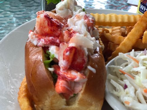 A lobster roll topped with fresh lobster meat and lettuce, served with crinkle-cut fries and coleslaw on the side.